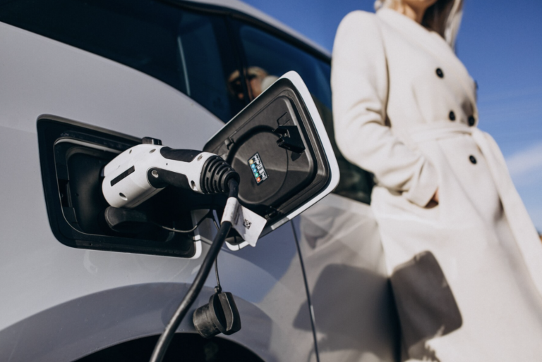 Photo d'une voiture électrique en tain de recharger avec une femme attendant contre la voiture