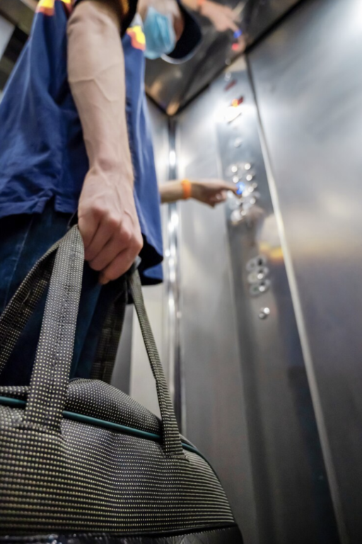 Un technicien tient un sac avec son matériel et appuie sur le bouton d'un ascenseur