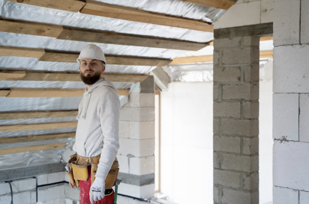 Photo d'un ouvrier regardant la caméra, sous des combles rénovées