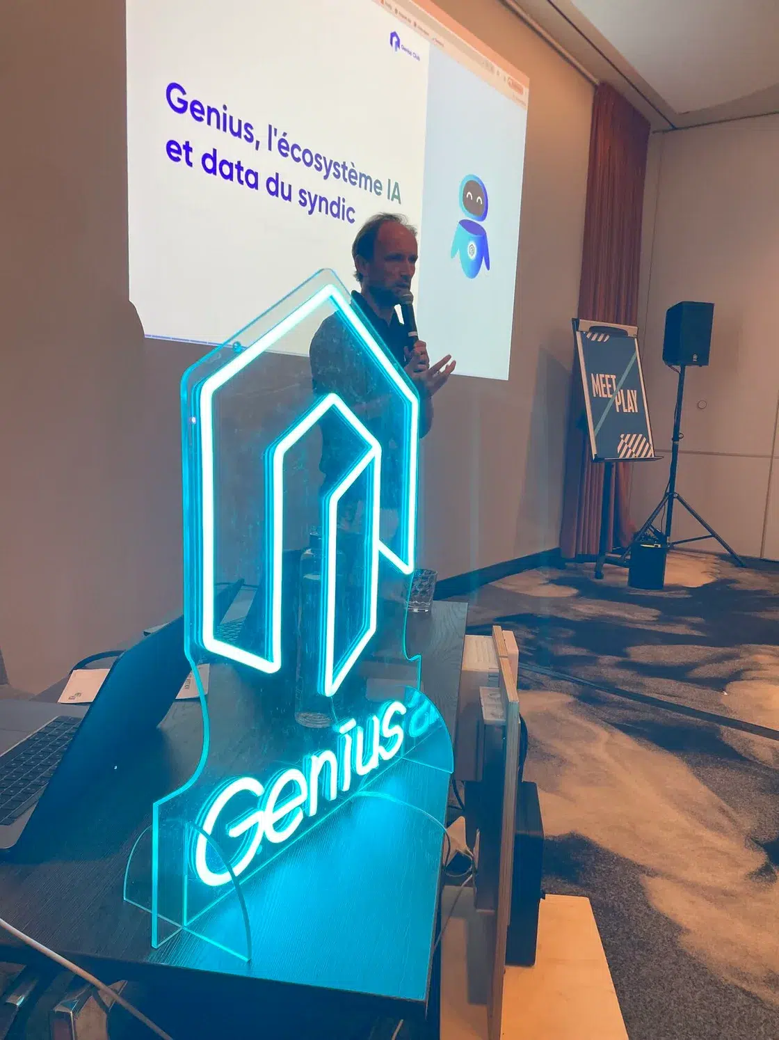 Prise de parole au micro devant la slide « Genius, l'écosystème IA et data du syndic » au Genius Club Paris